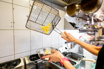 A chef’s hands using a deep fryer basket to drain freshly cooked fries over a pot in a commercial kitchen. The image captures the fast-paced environment and precision of culinary work