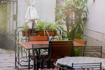 summer vivid time cafe patio space with chair and table furniture back street of old European town in sunny bright weather day with foreground blurred effect from flower pot