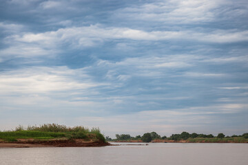 Serene river landscape of Madagascar under a dramatic sky with lush greenery along the banks during the day