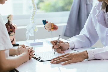 Asian male doctor consults with patient in clinic, reviews medical documents and uses stethoscope...
