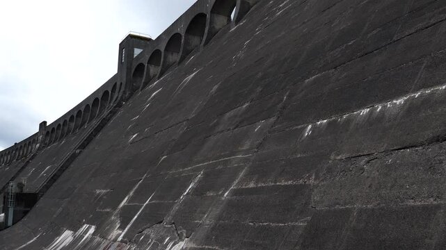 Downstream slope of Clatteringshaws Dam in Galloway Forest Park in summer, Scotland tilt down shot.
