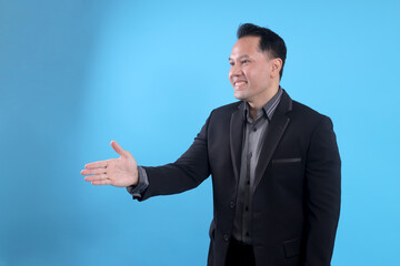 Male businessman in a suit stretching hand and shows a palm up gesture on a blue background. Concept of request and handshake.