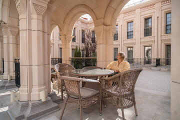Man, Patio, Building - A lone man sits at a table on a patio in front of a building.