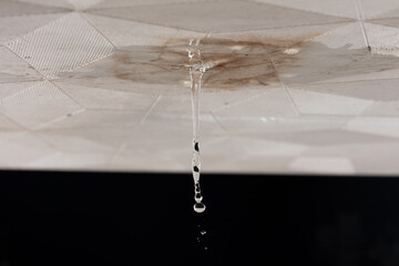 Ceiling Water leak from rain or broken pipe. House Water leaking on ceiling tile board and create dirty stain of flowing water, black background isolated