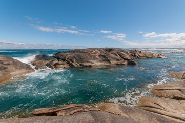 Western Australia, Green's Pool in Denmark, rocky coastline with clear water and distant waves under a partly cloudy sky.