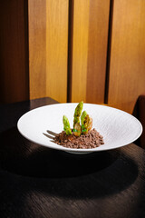 Green asparagus dish served on white plate with brown crumble on black table