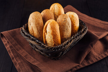 Freshly baked bread rolls lying in wicker basket on brown napkin