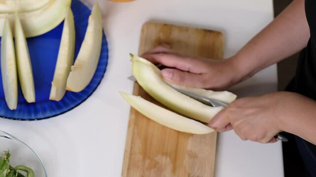 In a kitchen setting, hands cut a melon into slices, with a blue plate ready to serve the fruit. This photo illustrates the simplicity and benefits of incorporating fresh produce into daily meals.