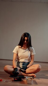 Young woman eating sushi burger with chopsticks while sitting in lotus position. Japanese food concept. Sushi burger in hands.Vertical vedeo 4K