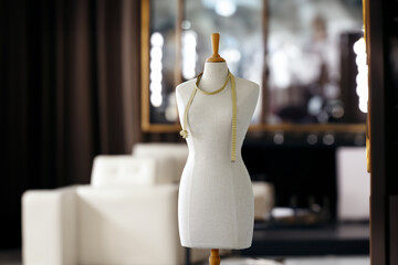 Elegant tailor dummy adorned with measuring tape, illuminated interior of a modern fashion design studio.