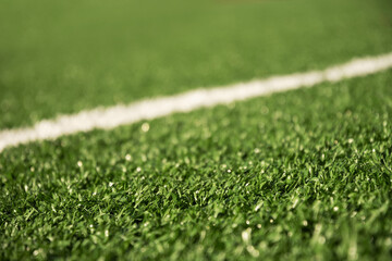 Artificial green grass with white stripe of soccer field. Outdoors. Summer. Close up.
