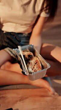 Young woman eating sushi burger with chopsticks while sitting in lotus position. Japanese food concept. Sushi burger in hands.Vertical vedeo 4K