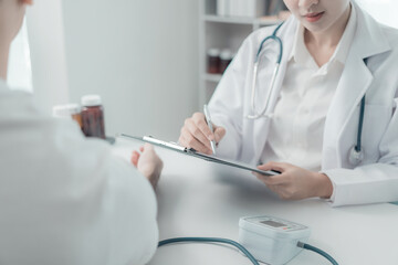 Asian female doctor and male patient discuss treatment with successful professional physician wearing white lab coat and stethoscope about injury