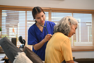 Healthcare professional in blue scrubs using a stethoscope to check breathing of an elderly female patient