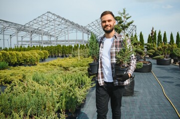 Male employee of garden shopping center inspects product. Department with potted plants, is...