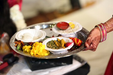 Indian pooja thali is a decorated plate used for rituals, containing a diya, incense sticks, kumkum, haldi, rice, flowers. It is essential for offering prayers to deities during religious ceremony.