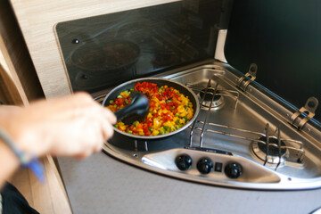 Person cooking mixed vegetables in a pan on a stove inside a motorhome