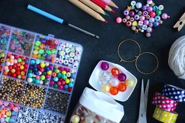 Colorful beads, coloring pencils, glitter, needles, string, hoop, tape and scissors on dark...