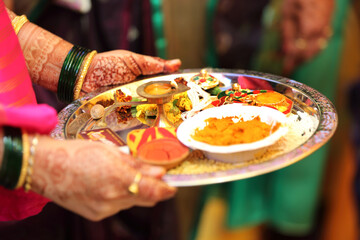 Indian pooja thali is a decorated plate used for rituals, containing a diya, incense sticks, kumkum, haldi, rice, flowers. It is essential for offering prayers to deities during religious ceremony.