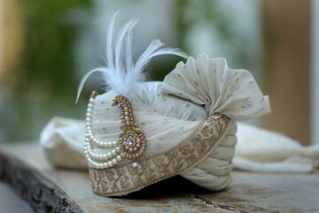An elegant white groom's turban adorned with intricate embroidery and pearls, symbolizing the regal attire of an Indian wedding. The scene exudes sophistication and cultural charm.