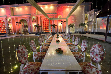 The image shows a beautifully arranged outdoor dining setup, featuring a long table with floral-patterned chairs under a canopy of string lights.