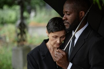 Side view of sorrowful Black man comforting grieving senior woman leaning on his shoulder at...