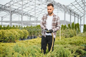 Young male gardener watering plants with a shower head and hose
