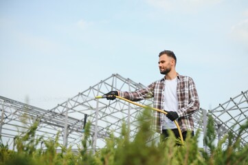 Young male gardener watering plants with a shower head and hose