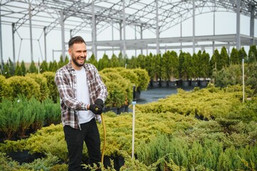 Young male gardener watering plants with a shower head and hose