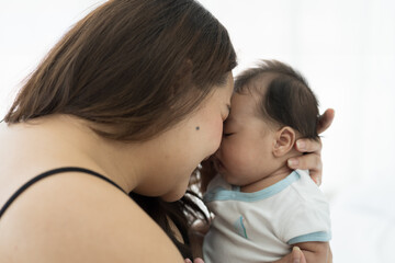Asian plus size mother embracing and carrying her newborn baby at home