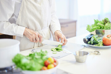 キッチンにて料理をするエプロンを着た日本人シニア女性