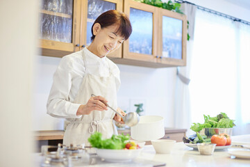 キッチンにて料理をするエプロンを着た日本人シニア女性