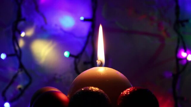 Una toma de cerca de una vela blanca con llama rodeada de bolas y varias luces con bombillos de varios colores en movimiento en la oscuridad