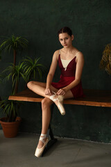 A ballerina laces her ballet shoes. A dancer puts pointe shoes on his feet.