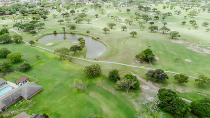 Golf course pond water runoff, sand trap, grassy fairways, club cars pathway in suburban country club recreational center near Hazel Park, Corpus Christi, Texas, upscale houses with pools, aerial