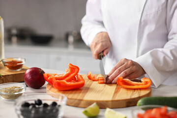 Professional chef cutting pepper at table in kitchen, closeup