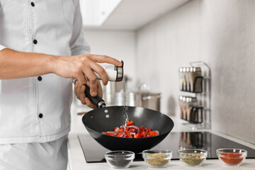 Professional chef adding salt into frying pan in kitchen, closeup
