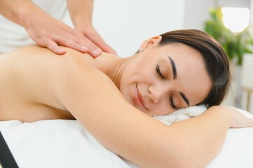 Obraz premium A young brunette woman receives a professional back massage in a spa salon. A beautiful naked lady in a towel with perfect skin gets a relaxing massage. The concept of luxury professional massage