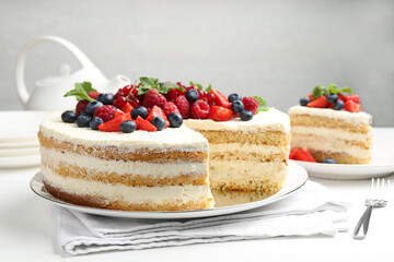 Tasty sponge cake with fresh berries and mint served on white table