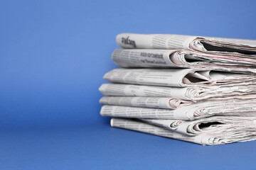 Stack of newspapers in different languages on blue background, space for text