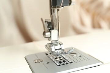 Sewing machine with beige thread on blurred background, closeup