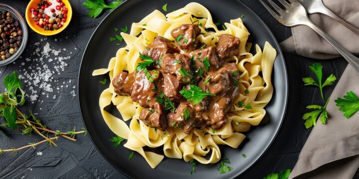 Beef stroganoff served with egg noodles and parsley on a stylish black plate