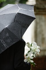 Vertical shot of unrecognizable person hiding from rain under black umbrella glistening with...