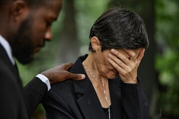 Medium shot of senior woman in black suit covering face with hand grieving over loss of loved one,...
