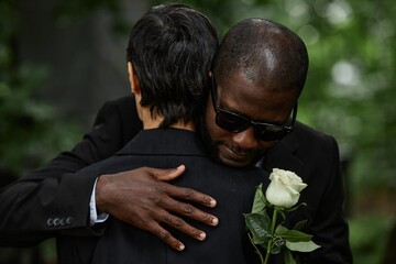 Medium shot of adult Black man in sunglasses hugging senior woman while grieving over loss of loved...