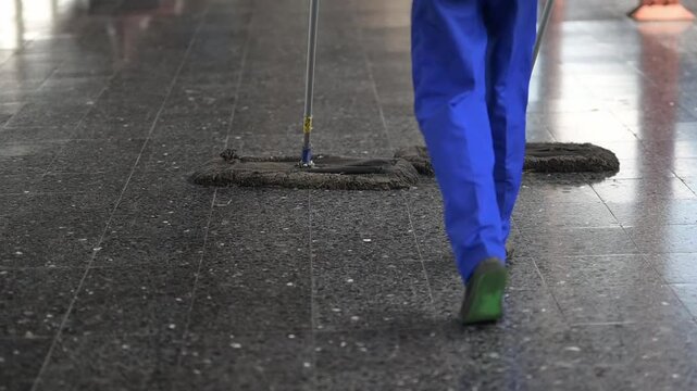 Janitor cleaning a shiny black tile floor with a mop