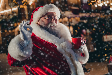 Photo of bearded man wear red warm costume hold mug hot tasty beverage cacao tea mulled wine okay symbol enjoy travel night city outdoor