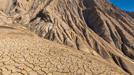 An imposing steep arid mountain with cracked and dry ground extending into the distance under clear blue sky emphasizing harshness.