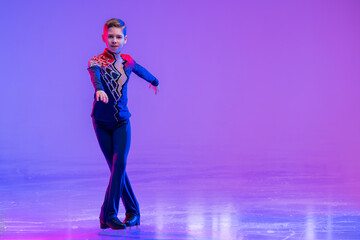 Boy figure skater skating on ice. With festive colored lilac lighting. © Maria Moroz