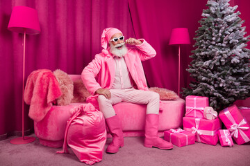 Photo of senior bearded male santa claus sit sofa cool boots fur coat fluffy nighty hat sunglasses pink new year celebration decor x-mas